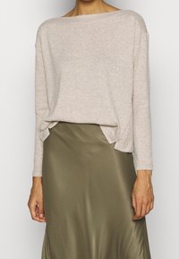 Pull beige texturé avec large encolure et manches longues, associé à une jupe lisse vert olive avec une légère fente.