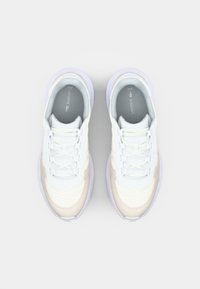 White and cream athletic shoes with textured fabric, flat laces, padded collar, and light rubber outsole. Lacoste logo on tongue.