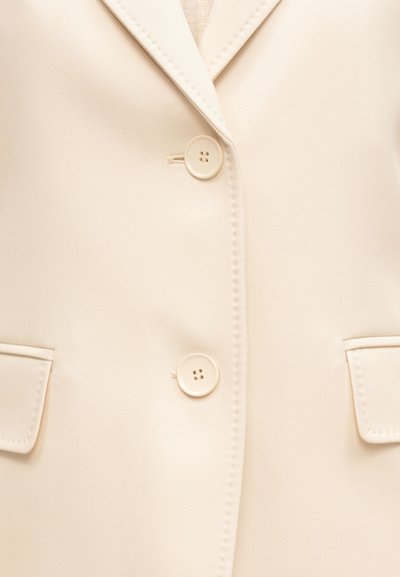 Μπεζ σακάκι σε κρεμ απόχρωση με δύο κουμπιά κλειστά, γιακά με εγκοπή και δύο εμπρόσθιες τσέπες με καπάκι ορατές.