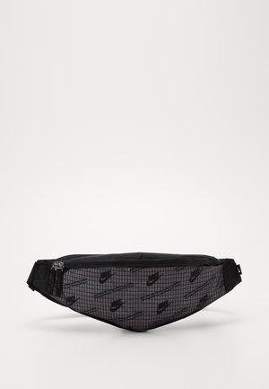Sac banane Nike noir et gris avec motif quadrillé, plusieurs logos et fermeture éclair sur fond blanc.