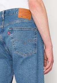 Jeans de denim azul claro com um patch de couro na cintura rotulado "Levi Strauss & Co." e uma etiqueta de logotipo vermelho no bolso de trás.