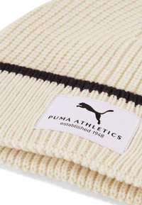 Berretto a maglia crema con trama a coste, caratterizzato da una striscia nera e un'etichetta bianca con la scritta "PUMA ATHLETICS" e il logo di un puma in salto.