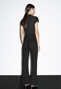 Zwart aangesloten top met korte mouwen, gecombineerd met hoge taille wijde broek, met een zachte textuur en naadloos ontwerp. Platte zwarte schoenen.