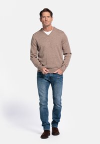Een koffiekleurige, gebreide v-hals trui gecombineerd met een spijkerbroek en donkerbruin suede laarzen. De outfit toont een casual, getailleerd silhouet.