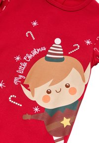 Un mono de algodón rojo con un elfo de dibujos animados que lleva un sombrero a rayas, bastones de caramelo y el texto "Mi pequeño Christmas", todo sobre un fondo festivo.