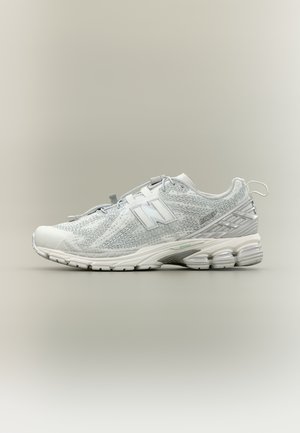 Zapatilla deportiva blanca New Balance 1906R con parte superior de malla, suela acolchada, cinta para tirar en el talón y logo en relieve en el lateral y la lengüeta.