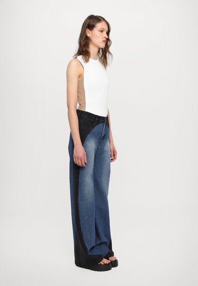 White and beige tank top with ribbed texture; wide-leg jeans in gradient blue denim with black accents; chunky black platform sandals.