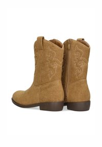 Botas de tobillo de ante marrón con punta redondeada, tacón bajo, diseño de costuras intrincadas y cierre de cremallera lateral. Superficie texturizada en todo su alrededor.