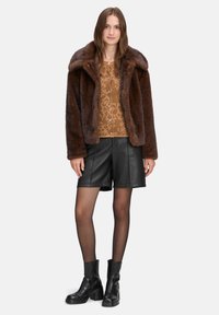 Brun faux fur frakke med en bred krave, parret med en tan mønstret top, sorte læder shorts og kraftige sorte ankelstøvler.
