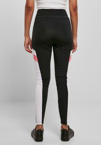Musta-valkoiset legginsit vaaleanpunaisilla yksityiskohdilla. Korkea vyötärö, tiukka muotoilu, sileä pinta. Sivut on varustettu värilohkoilla.