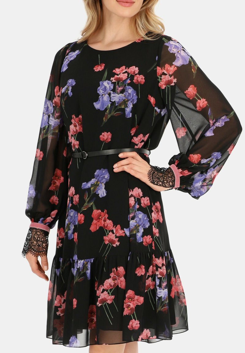 Czarna sukienka w kwiaty z purpurowymi i czerwonymi wzorami, z długimi przezroczystymi rękawami, koronkowymi akcentami przy mankietach i falbaniastym dołem.