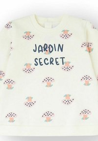 Camisa de manga larga color crema con patrones de hongos moteados en rosa y negro, y el texto "JARDIN SECRET" en azul oscuro en el frente.