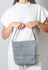 Borsa in suede grigia con una texture trapuntata, dotata di manico a catena. La borsa ha una finitura morbida e opaca e una forma rettangolare strutturata.