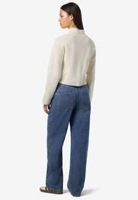 Pull en maille côtelée crème avec un col montant et des manches raglan, associé à un jean en denim bleu ample avec des poches arrière.