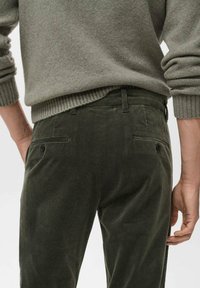 Pantalones de pana verde oliva con textura acanalada, con dos bolsillos traseros y un corte recto, combinados con un suéter gris.