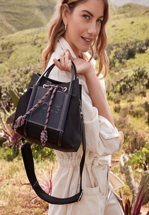 Black bucket bag made of smooth material, featuring a drawstring closure with patterned cords, and a detachable strap. Accented logo on front.