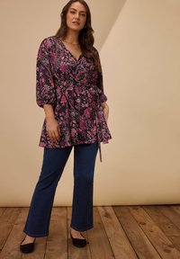 Top con stampa floreale nera con accenti rosa, caratterizzato da un design avvolgente, scollatura a V e maniche a palloncino, abbinato a jeans a zampa d'elefante blu scuro.