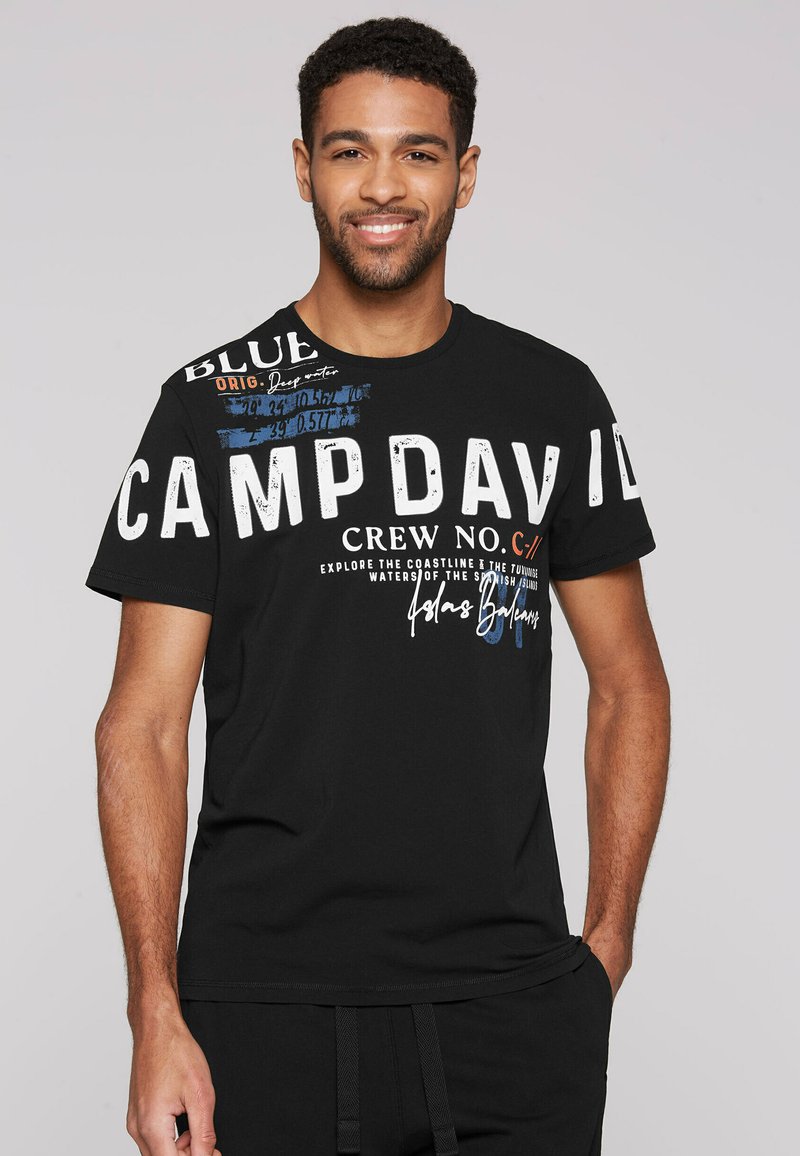 Camiseta de algodón negra con un atrevido texto blanco "CAMP DAVID" y varios gráficos y textos de colores. Mangas cortas, cuello redondo, corte relajado.