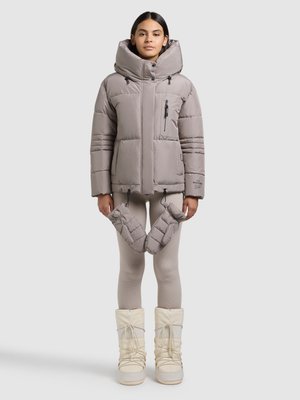 Kurtka puchowa w jasnoszarym kolorze z wysokim kołnierzem, kieszenią na zamek i troczkiem. Noszona z dopasowanymi szarymi legginsami i białymi śniegowcami.