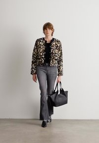 Panterprint nep bontjas, zwarte top, grijze flared jeans, zwarte handtas en schoenen. Effen achtergrond, model loopt vooruit.