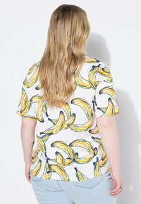 Camisa de manga corta en algodón blanco con un estampado colorido de plátanos en amarillo y azul. Corte relajado con cuello redondo y textura suave.