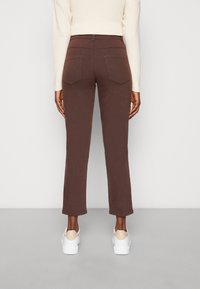 Pantaloni dritti marroni in misto cotone, con tasche posteriori e una texture liscia, abbinati a sneakers bianche.