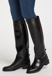 Boots de piele negre până la genunchi, cu o textură netedă, un fermoar pe lateral și un toc jos. Designul are accente minime.