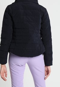 Námořnická prošívaná bunda s kanálkovým prošíváním, vysokým límcem a přiléhavým pasem. Vyrobena z lehkého materiálu, navržena pro teplo a pohodlí.