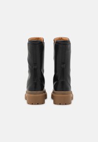 Stivali ankle in pelle nera con suola in gomma color tan, caratterizzati da una texture liscia, punte arrotondate e linguette sul retro per una facile calzata.