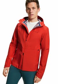 Giacca impermeabile rossa con chiusura a zip, cappuccio regolabile e tasche laterali. Presenta un rivestimento interno viola a contrasto e un logo.