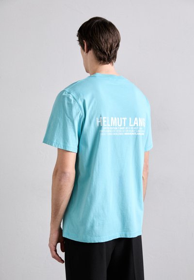 Tirkizna pamučna majica s kratkim rukavima i ravnim krojem. Na leđima se nalazi bijeli logo "HELMUT LANG" s natpisom ispod.