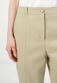 Μπεζ παντελόνια με ραφή, απαλό υφή και ελαφριά γυαλάδα, με ζώνη στη μέση και ορατό κούμπωμα στο εμπρός μέρος. Διαθέτουν ακριβή ραφή.