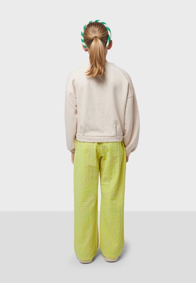 Light beige oversized sweatshirt with long sleeves paired with textured, bright lime green, wide-legged pants. Green striped headband worn.