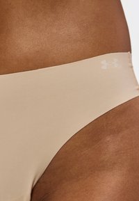 Κοντινό πλάνο ενός ατόμου που φορά αόρατα μπεζ εσώρουχα με διακριτικό λογότυπο Under Armour στη μέση.