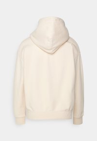 Sudadera con capucha de color crema, con cordón ajustable, corte holgado, puños y dobladillo acanalados. Textura suave con detalles mínimos de costura.