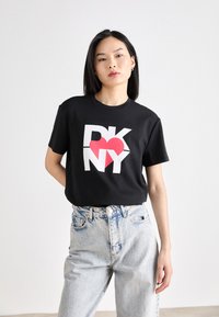 Svart bomullst-skjorte med store hvite "DKNY"-bokstaver og et rødt hjerte i midten, kombinert med lyseblå høytaljede jeans.