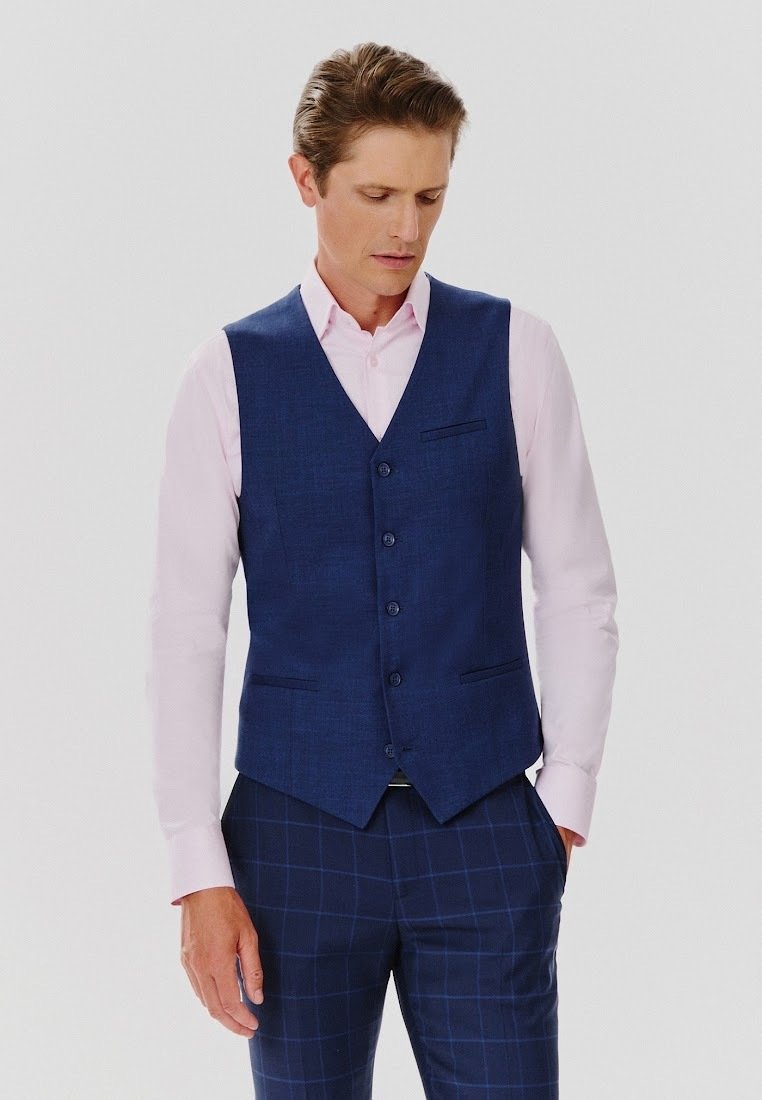 Granatowa kamizelka z teksturowanej tkaniny o dopasowanym kroju, z pięcioma guzikami i dwiema kieszeniami, zestawiona z jasnoróżową koszulą z kołnierzykiem.