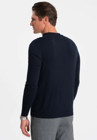 Navyblauer Strickpullover mit Rundhalsausschnitt, langen Ärmeln und geripptem Saum. Glatte Textur, figurbetontes Design, von hinten betrachtet.