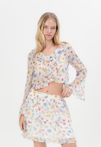 Top court en chiffon à motif floral avec un décolleté à volants, de longues manches évasées, et une jupe mini à plusieurs niveau assortie avec un motif de fleurs pastel.