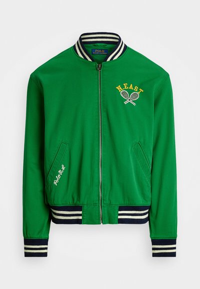 Casaco bomber verde com um colarinho listrado azul canelado. Apresenta o bordado "N.E.A.S.T." e raquetes de ténis. Dois bolsos laterais.