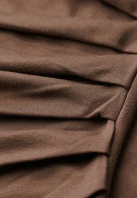 Brązowa tkanina o gładkiej fakturze i subtelnym prążkowaniu. Materiał jest zebrany w fałdy, co tworzy miękkie linie i głębię.