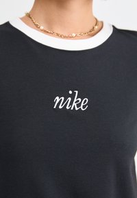 Fekete póló fehér kerek nyakkivágással és fehér hímzett "nike" logóval a mellkason, puha anyagból készült, sima textúrával.