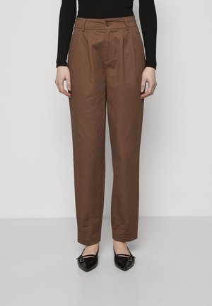 Brown pleated trousers with a high waist and button closure. Smooth fabric with a tailored fit, paired with pointed black flats.
