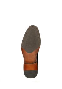 Suela negra de zapato con acento en el talón de cuero marrón, fondo de goma texturizada, costuras en contraste y una forma ligeramente curvada.