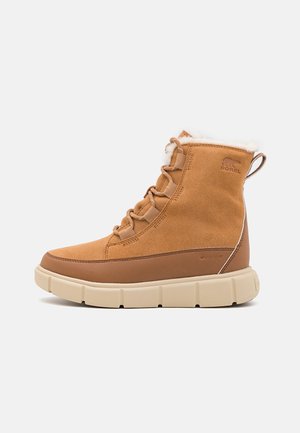 Tan vandtæt vinterstøvle med beige tyk sål, snørelukning foran, fårskindsfór og logo på anklen, vist i siddeprofil.