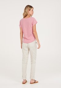 Blusa de manga corta, con estampado rosa y cuello redondo, combinada con pantalones beige claros con dobladillo enrollado y sandalias marrones.
