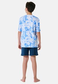 T-shirt z krótkim rękawem w kolorze jasnoniebieskim i białym w stylu tie-dye, połączony z ciemnoniebieskimi szortami. Posiada luźny krój i miękką tkaninę.