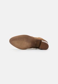 Chaussure en suede marron avec un bout rond, tige texturée et semelle en cuir lisse. Présente un logo embossé sur la semelle extérieure.