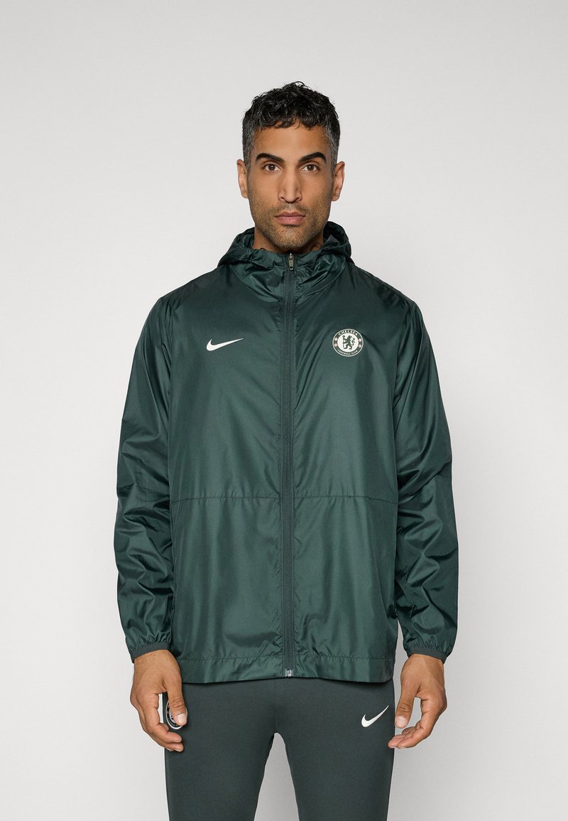 Dark green Nike windbreaker jacket with a hood, featuring a zip front, elastic cuffs, and a Chelsea FC badge on the left chest.