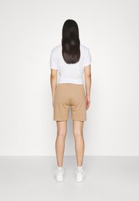 Kortärmad vit t-shirt och beige svettshorts med elastisk midja, kombinerat med vita sneakers. Enkel design, minimalistisk stil.